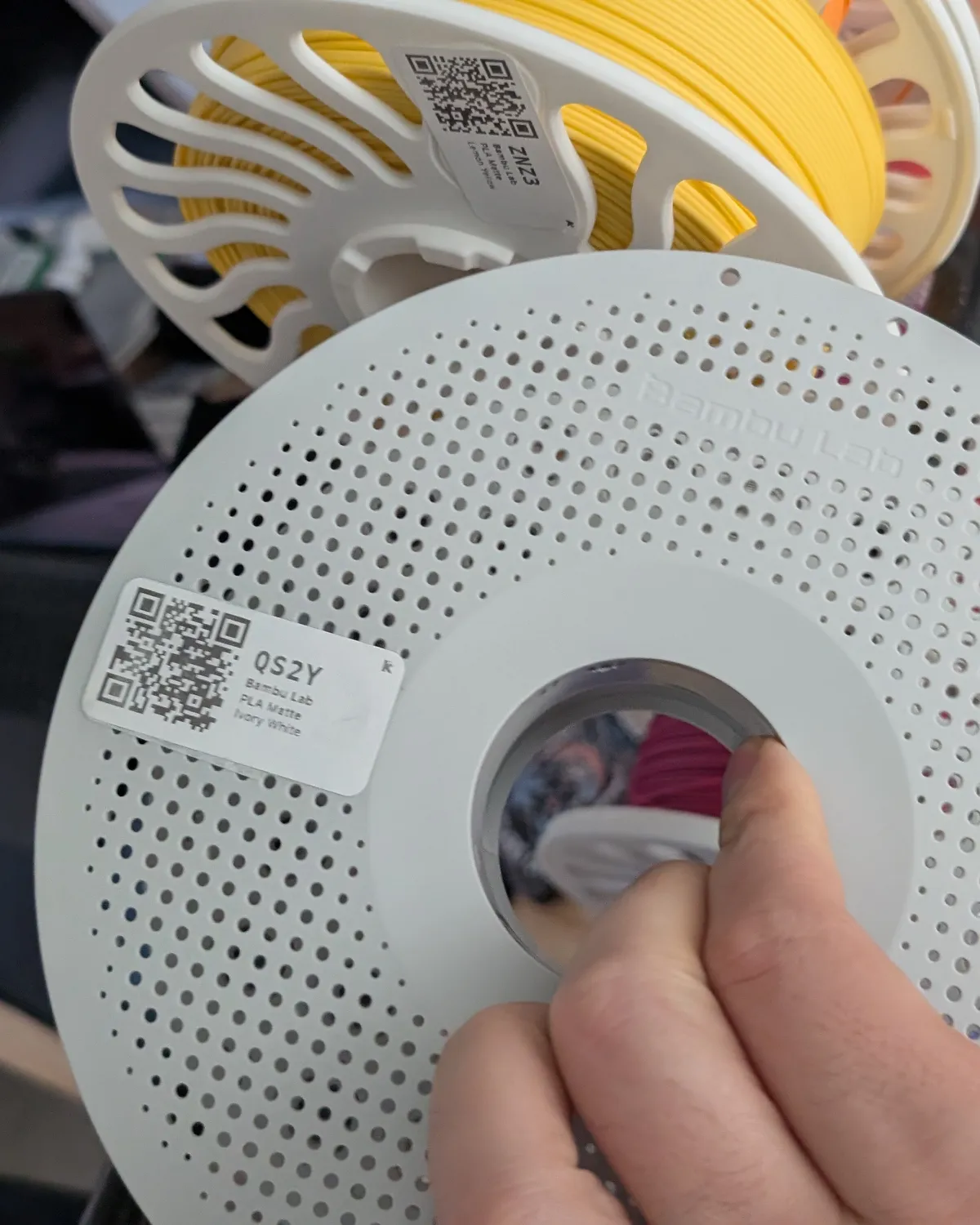 Hand pulling a QR-labelled spool from the filament rack